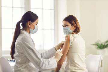 Professional nurse giving vaccine to young woman during vaccination campaign at health center