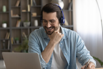 Happy millennial man in headphones and glasses study online or take training on computer on web....