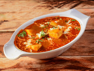 Paneer Butter Masala or Cheese Cottage Curry, served over a rustic wooden background, selective focus