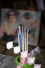 Brushes and paints for painting in a jar. Nearby is a fragment of a painted picture. On black pine boards.
