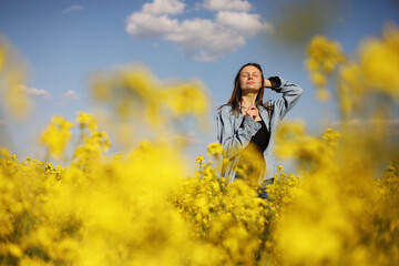 young beautiful woman in a field with yellow blooming rapeseed. girl in yellow floral field, rapeseed plantation, summer vacation concept