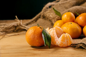 Fresh juicy tangerines or mandarins with green leaves on sack cloth and wooden table.