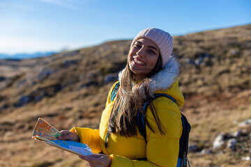 Portrait of smiling woman hiking and holding a geographical map at the top of the mountain. - obrazy, fototapety, plakaty