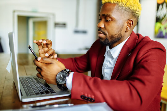 african american person sitting at office typing message note on phone near laptop