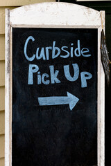Sign for Curbside Pick Up on an old weathered chalkboard with blue chalk. 