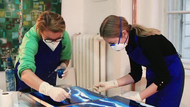 Two artists make a painting with blue epoxy material. Making a work of art in a workshop. Respiratory protection with a mask. Lesson at art school.