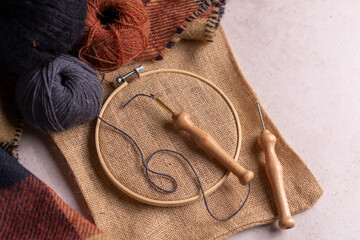 Punch needle tool composition with a burlap fabric in a embroidery hoop and a threaded needle with...