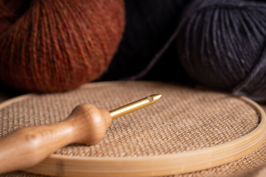 A golden magic needle for embroidery on a jute fabric and some wool balls in the background.