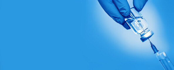 Vaccine in a bottle with a syringe on a blue background.The concept of medicine, healthcare and science.Coronavirus vaccine.Copy space for text.Banner