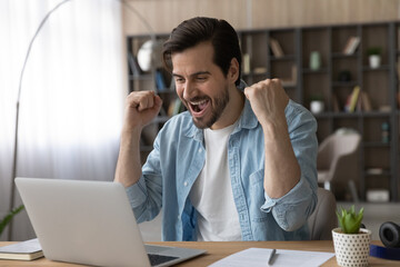 Excited young Caucasian man look at laptop screen feel euphoric celebrate online lottery win. Overjoyed millennial male triumph reading good news on computer, get promotion email letter. Luck concept.