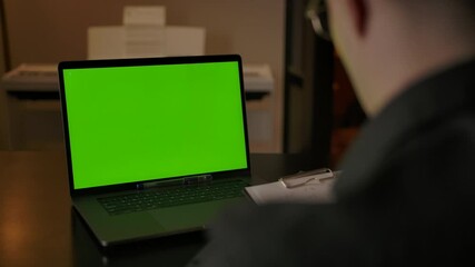 Young studying caucasian male writing task solution on tablet PC from laptop green screen with Your content, ready for tracking. Online learning mathematics at home in cozy interior. - Powered by Adobe