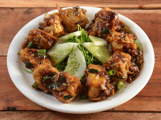 Paneer Manchurian is Indo Chinese cuisine dish, Paneer cubes tossed with tomatoes, onions, spring onions, sesame seeds and soy sauce. served over a rustic wooden background, selective focus