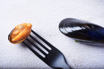 Mejillón cocido y pinchado con un tenedor sobre un fondo blanco, convista cenital