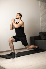 Athletic man doing lunge forward. Sport at home concept. Strong man stretching legs before workout. Healthcare concept. Male sportsman in black sportswear. Fitness or yoga.
