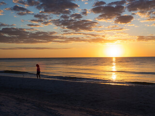 Young woman walking on a Gulf of Mexico beach at St. Pete Beach, Florida at sunset with a dramatic orange sunlit sky.