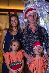 Happy family with two daughters standing by Christmas tree holding gift box present. Merry Christmas and happy holidays