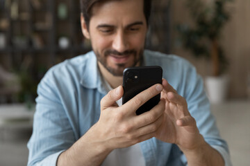 Obraz na płótnie Canvas Crop close up of happy millennial male look at cellphone screen browse surf wireless internet on gadget. Smiling young Caucasian man use smartphone texting or messaging online on device.