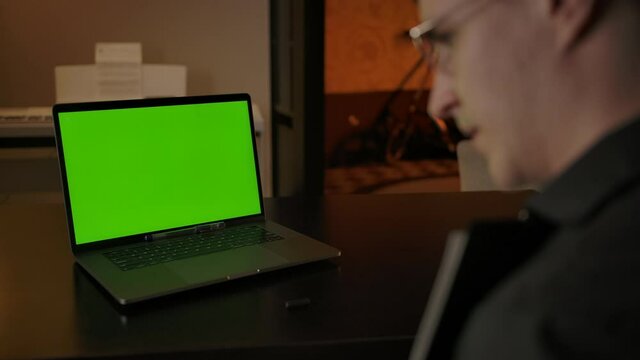 Back view of male, explaining equations on text tablet behind green screen with online conference call from home. Dolly shot ready for keying, tracking and replacing content.