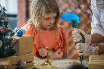 Little child decorating Christmas biscuits and gingerbread cookies in kitchen together with chef. Kids cooking class. Merry Christmas and happy holidays concept