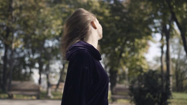 Side view of smiling gorgeous sportswoman shaking hair in sunlight outdoors. Happy relaxed Caucasian woman enjoying sunny summer day after training. Sport and workout concept.