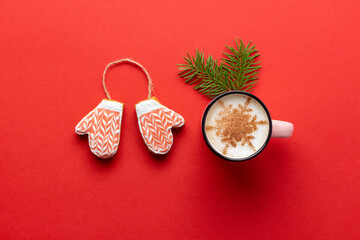Cup of cappuccino decorated with snowflake near gingerbread mittens on red background