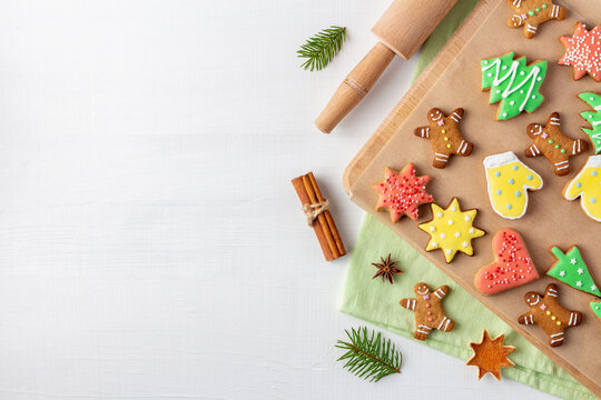 Christmas cookies with icing on cutting board near rolling pin on white wooden background