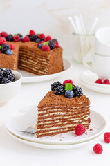 Chocolate honey cake with cream and fresh berries on top on a white plate on a light concrete background. Copy space.