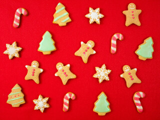 Fototapeta na wymiar Variety shapes of Christmas cookies: gingerbread man with surgical protective mask, Christmas tree, snowflake, candy stick. Homemade bakery on red background. Flat lay. Christmas coronavirus.