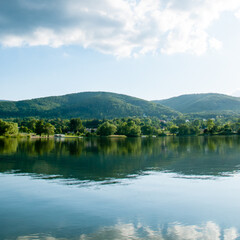 G&oacute;ry porośnięte lasem odbijające się w tafli wody jeziora. Nad g&oacute;rami niebo i chmury.