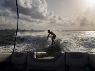 Back lit shot of man wake surfing behind boat at Miami Beach