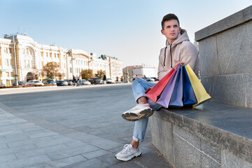 Tourist guy is resting with shopping bags and souvenirs on city background.