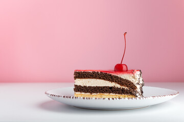 Piece of chocolate vanilla cake with maraschino cherry. Side view cake on pink background.