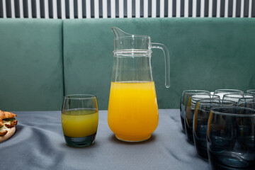 Glass fresh orange juice and tall jug of fruit drink on gray table