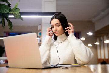 Cute woman in headphones working typing on laptop while sitting at desk in office at workplace. Enjoy the e-learning process, easy and convenient use of the app, listen to music during the working day