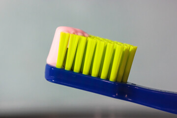 Blue toothbrush with green bristles close-up, pink toothpaste. Dental hygiene and care products from the dentist