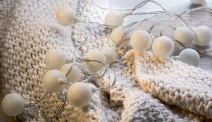 New Year's glowing lights on a white knitted scarf. Winter Christmas decor. Festive atmosphere. Warm colors, soft focus.