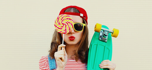 Summer portrait of young woman with lollipop and green skateboard wearing a baseball cap on a white background © rohappy
