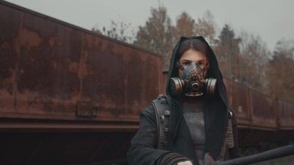 Woman in grunge clothes and gas mask with burning torch in her hand standing by rusty train carriage and looking into camera. Dystopia, female survivor in abandoned city. Post apocalyptic world - Powered by Adobe