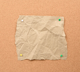 brown piece of torn paper pinned with iron buttons on a brown cork board