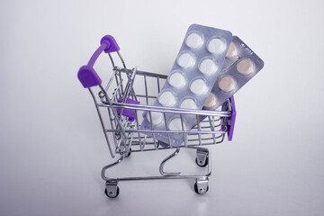 Mini decorative shopping cart with two blisters of tablets on white background.