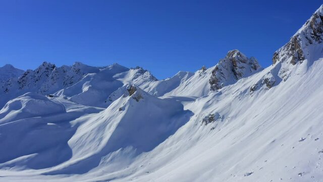 Mountain in winter - Drone flying above mountains covered with fresh snow in Tignes - Val d'Is&egrave;re, with a blue sky and a peak in background