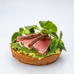 Bagel with tuna and greens on white background.
