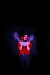 Female magician makes show with soap bubbles and smoke, an illusionist in theatrical clothes, on black wall. Woman actress in stage costume and top hat on her head. Concept of performance. Copy space
