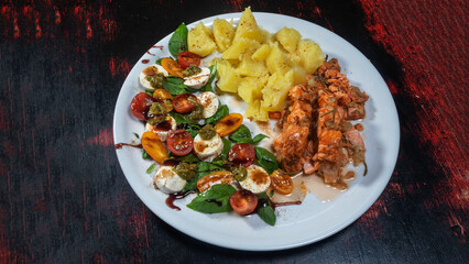 Boiled potatoes, fresh salad and roasted salmon on white plate. Dark wooden background. Cuisine concept.