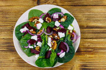 Tasty spinach salad with boiled beetroot, feta cheese, walnut and red onion on wooden table. Top view. Healthy vegetarian food