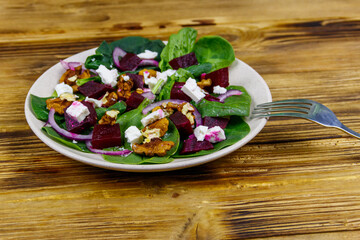 Tasty spinach salad with boiled beetroot, feta cheese, walnut and red onion on wooden table. Healthy vegetarian food