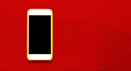 Top view of yellow cell phone with isolated black screen that contrasts with red background with wood texture and ample copytext space