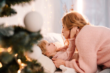 Fototapeta na wymiar Mom kisses her daughter who lying in bed near christmas tree