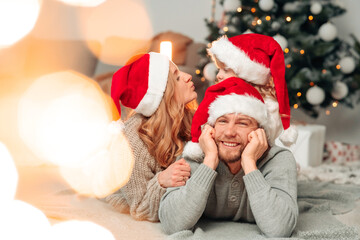 Family in santa claus hats lie on the floor of christmas decorated room