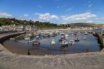 Lyme Regis harbour, full of boats, on a sunny spring April day, with bright blue sky and a few light fluffy clouds. Dorset, UK.